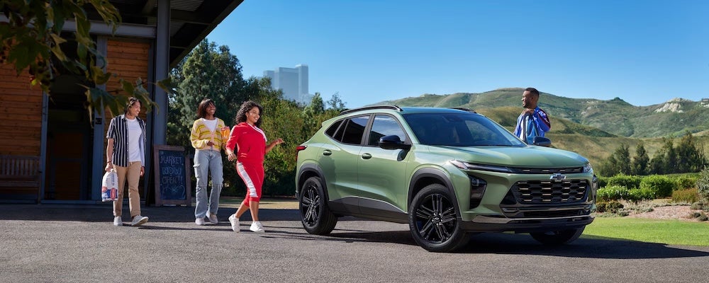 Four people standing outside a green 2026 Chevrolet Trax SUV with mountains in the background