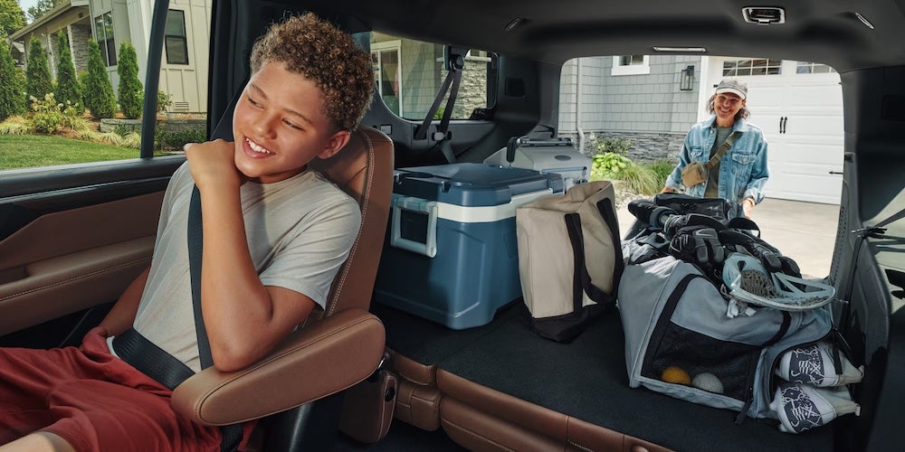 A child seated in the 3rd row of a Chevy Suburban while his mom packs the trunk