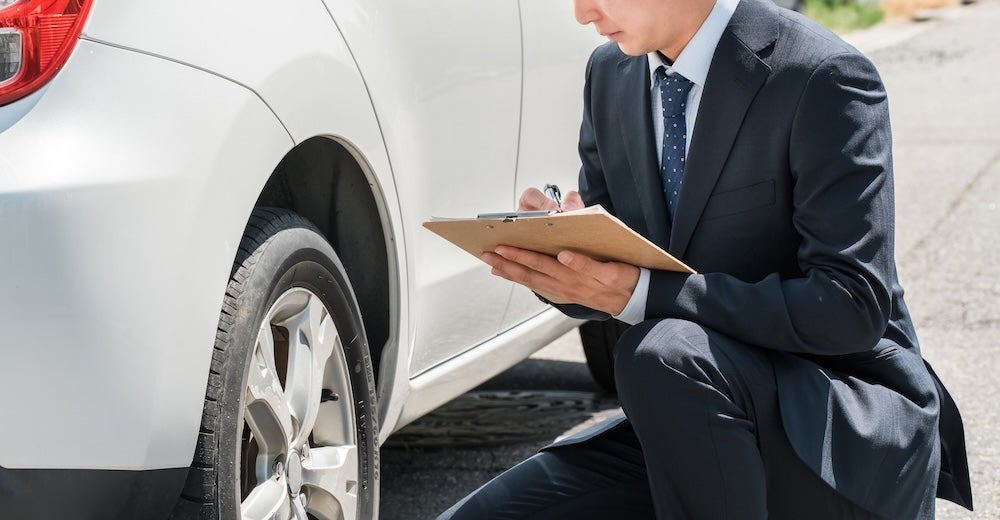 A person in a suit inspecting a white car
