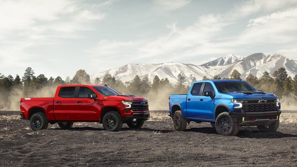 Two Chevy Silverado trucks, one red and one blue, parked near mountains