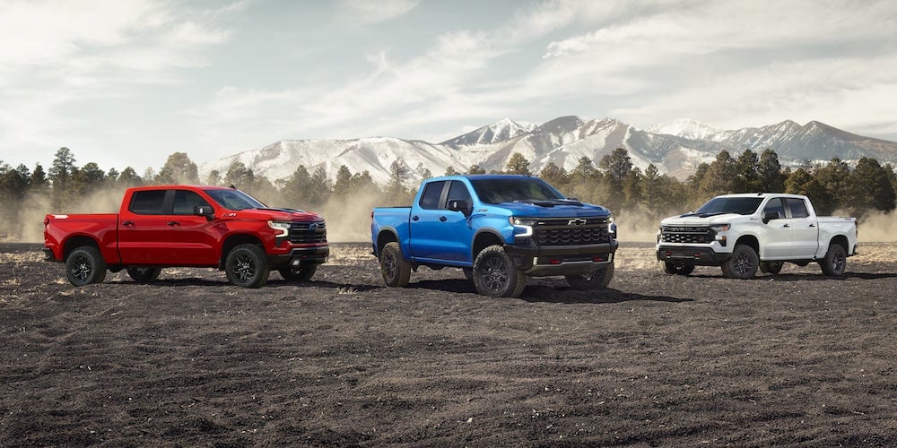 Three 2026 Chevrolet Silverado pickup trucks parked on a dirt field
